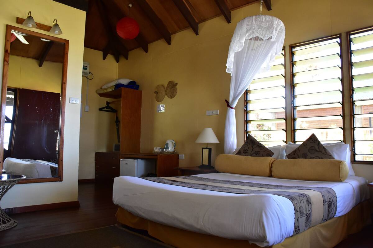 Une chambre à coucher bien rangée, avec un lit, une table de chevet, une lampe et un miroir.