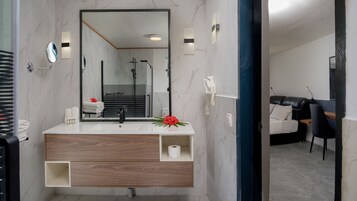Un baño moderno con tocador de mármol, un espejo grande y una zona de ducha visible a través de la puerta de cristal.