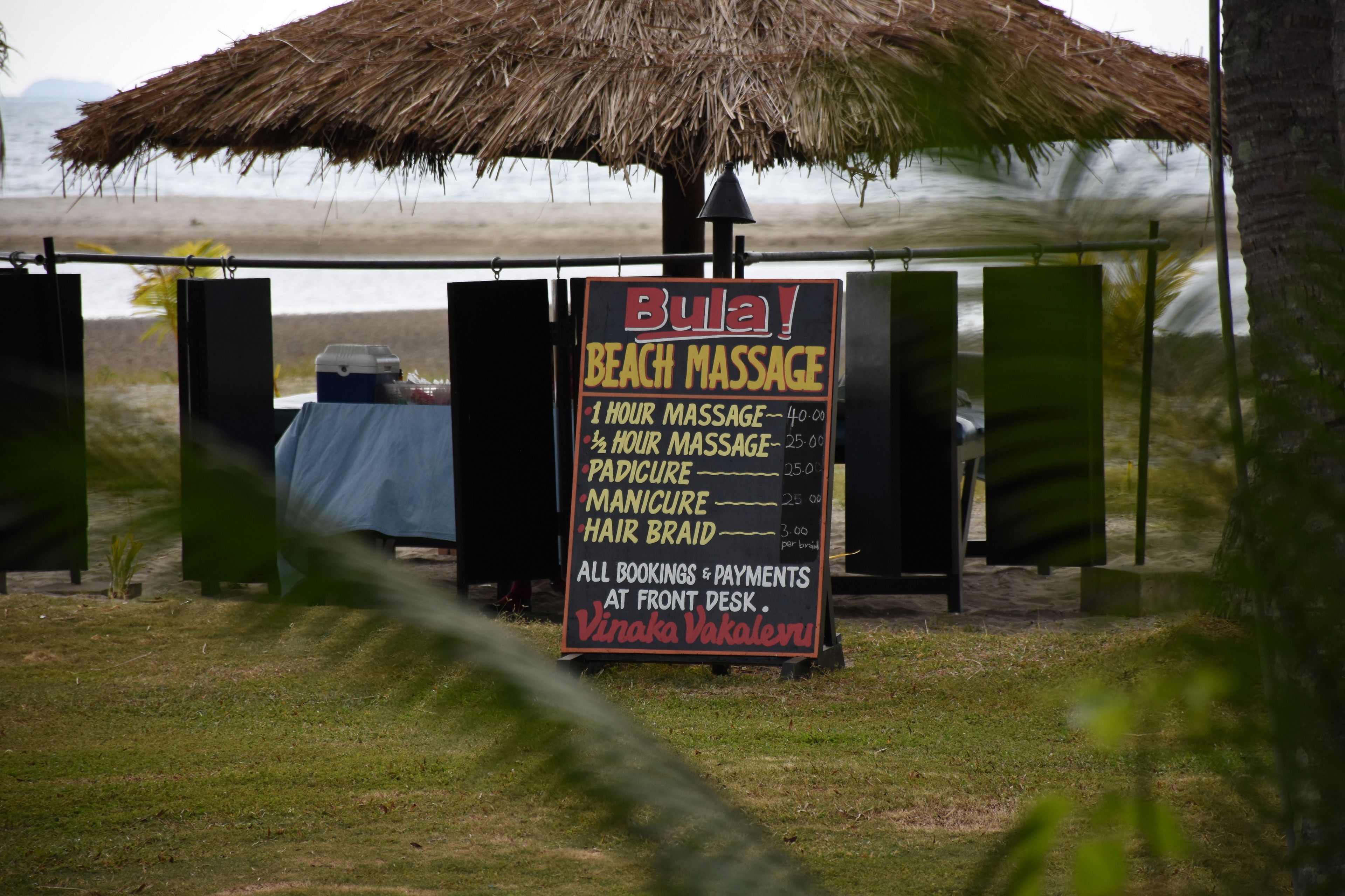 A beach massage service sign with prices and services listed.