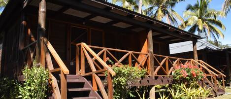 A wooden building with a porch and stairs, surrounded by tropical plants and palm trees.