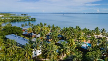 Un resort tropical con varias edificaciones tipo bungalow, una piscina y vista al océano.