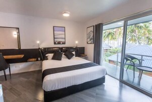 Habitación de hotel moderna con una cama grande, un escritorio y un balcón con vista a palmeras.