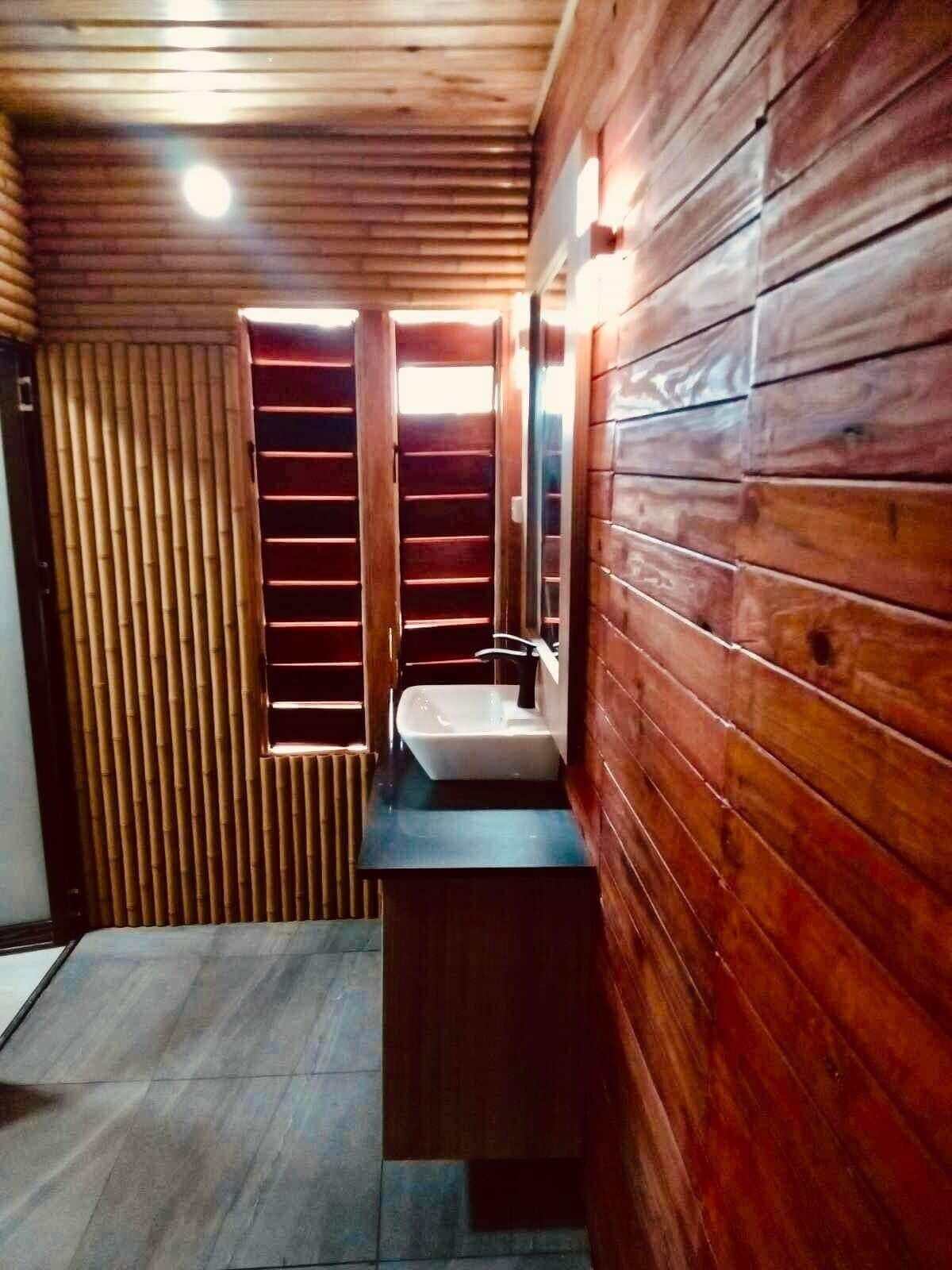 A wooden cabin bathroom with a built-in sink, a mirror, and a window.