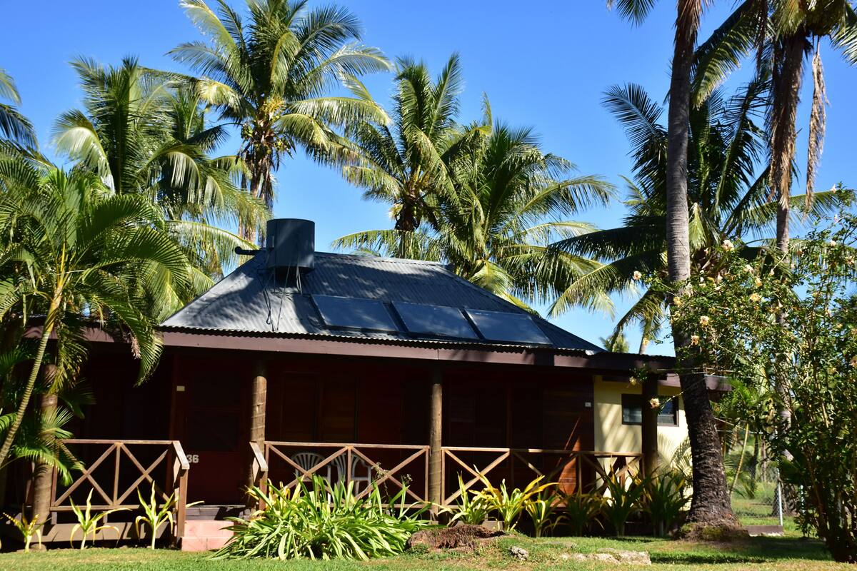 Un bâtiment d’un seul étage, doté d’un toit en pente, entouré de palmiers et de verdure.