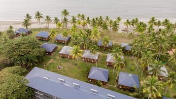 An aerial view of a resort with multiple bungalow-style buildings, palm trees, and a beach in the background.