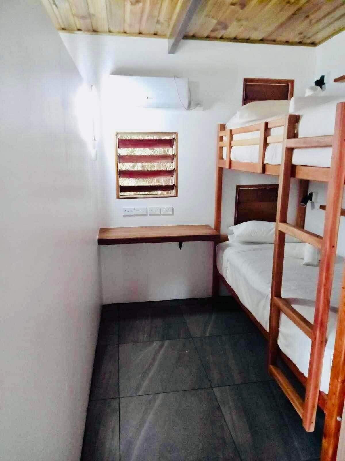 A compact room with bunk beds, a small desk, and a window with blinds.