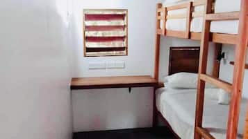 A compact room with bunk beds, a small desk, and a window with blinds.