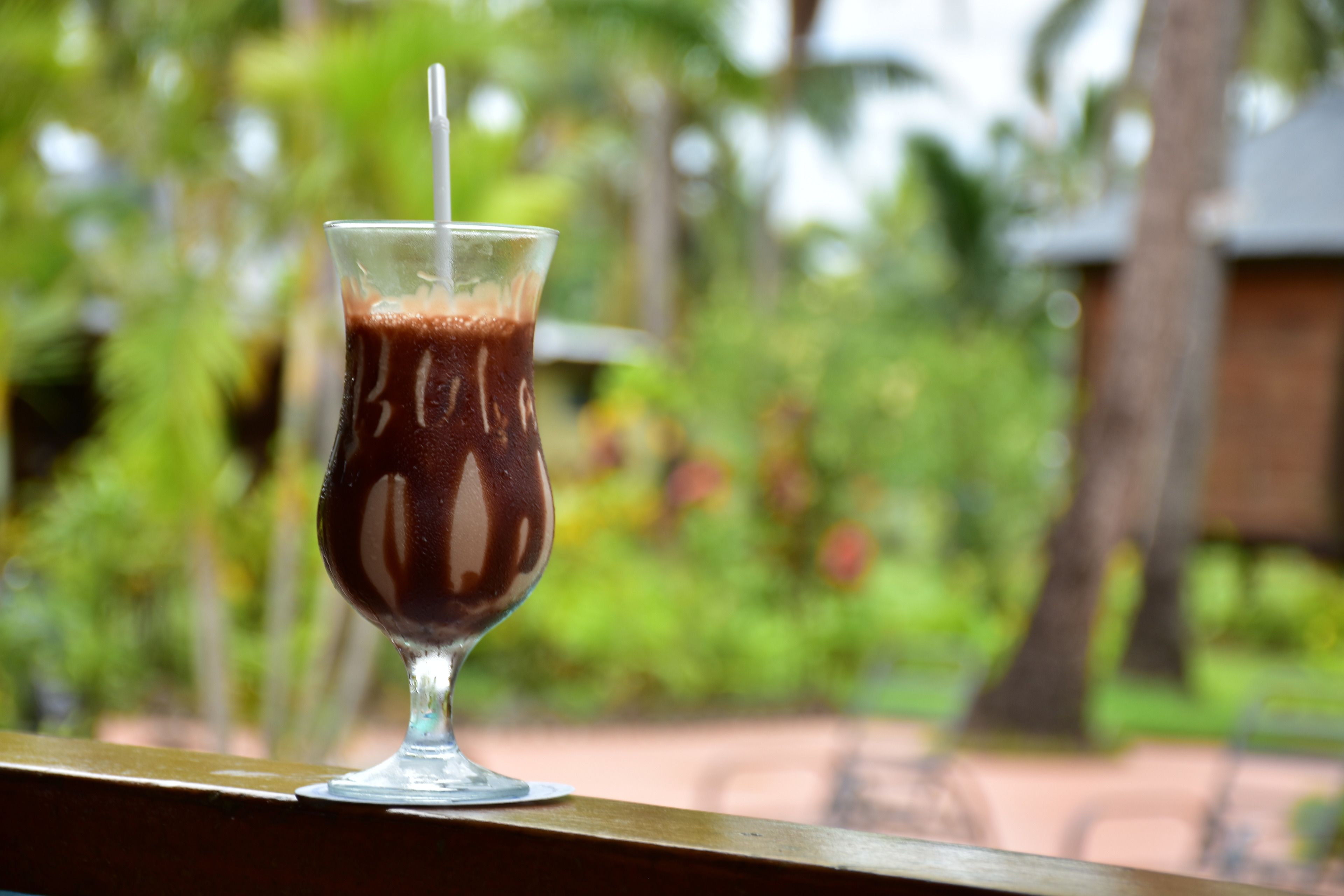 Um copo de café gelado com canudo sobre um apoio de madeira.