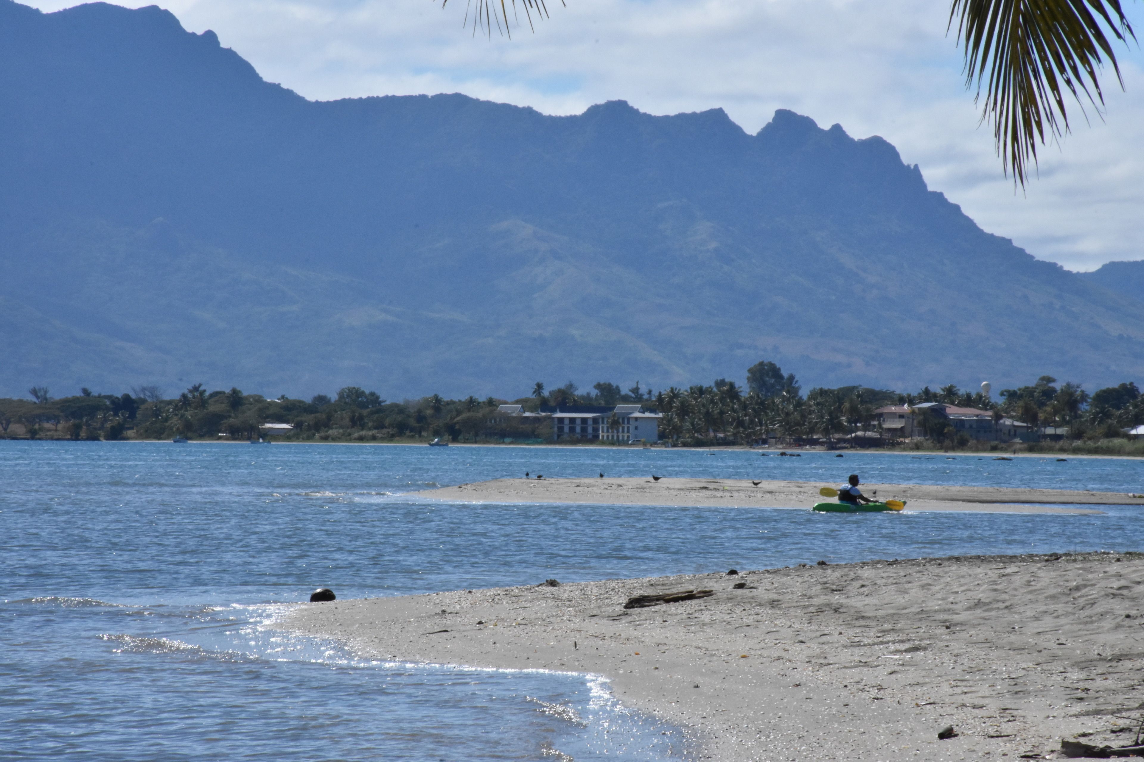 A beach with a kayak, a sandy shore, and mountains in the background.