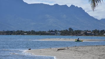 Una playa con kayak, orilla arenosa y montañas al fondo.