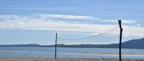 A beach volleyball net set up on a sandy beach with a clear view of the sea and distant mountains.
