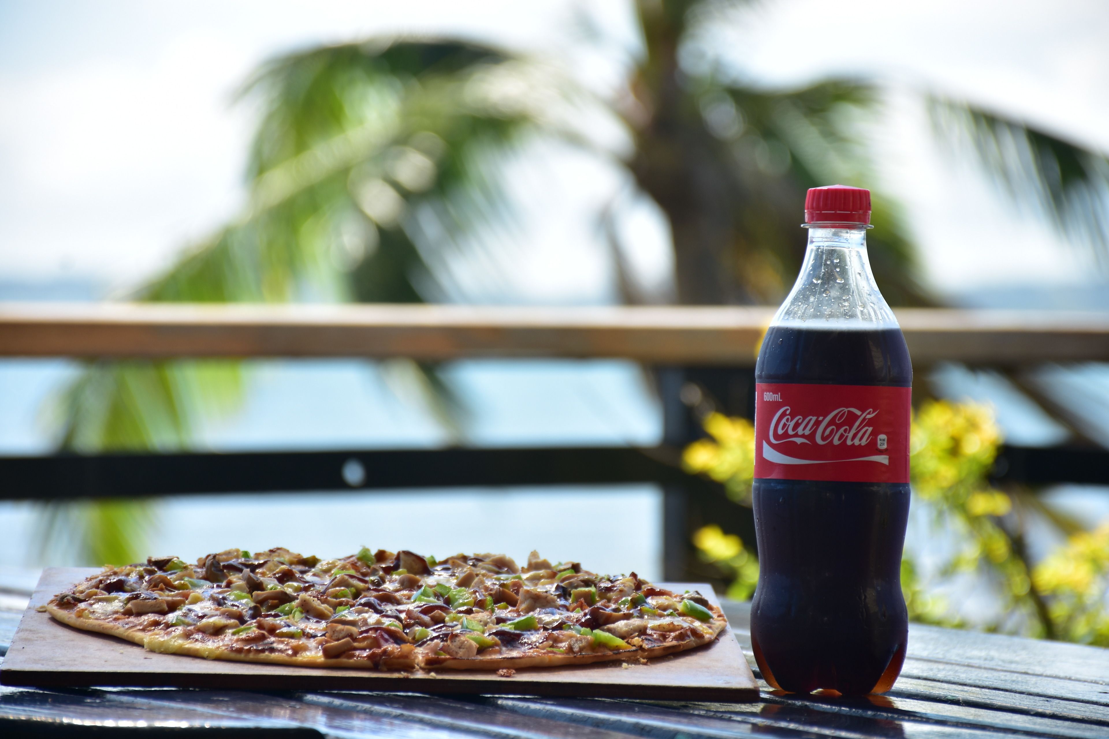 A pizza on a wooden board with a bottle of Coca-Cola beside it.