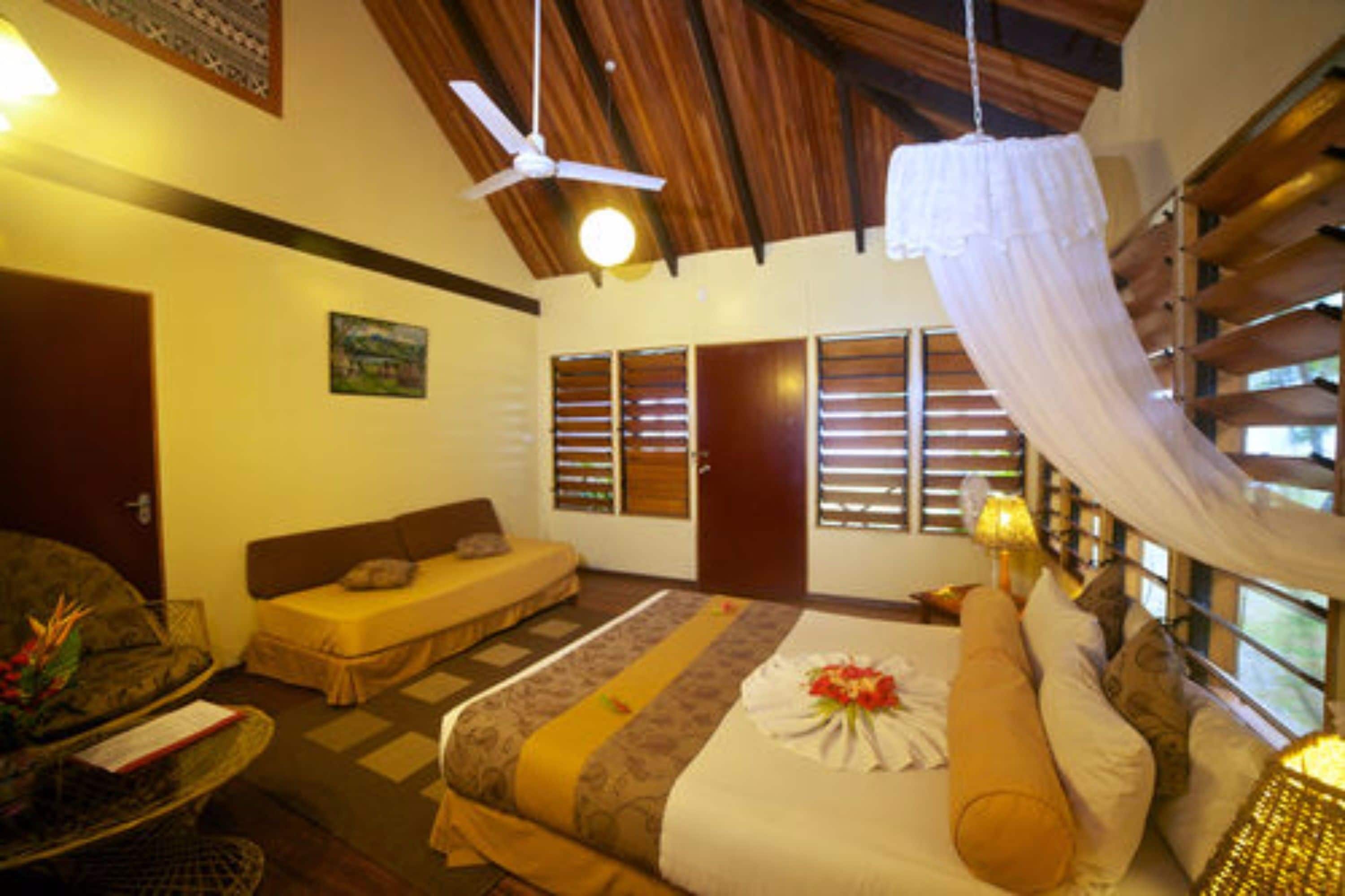 Una habitación con cama, sofá, ventilador de techo y ventana con persianas.