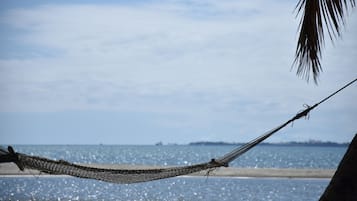 Een hangmat gespannen tussen twee bomen aan een strand, met uitzicht op de oceaan.