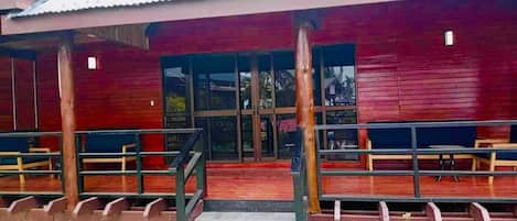 A building with a red exterior, large glass doors, and a covered outdoor seating area with benches.