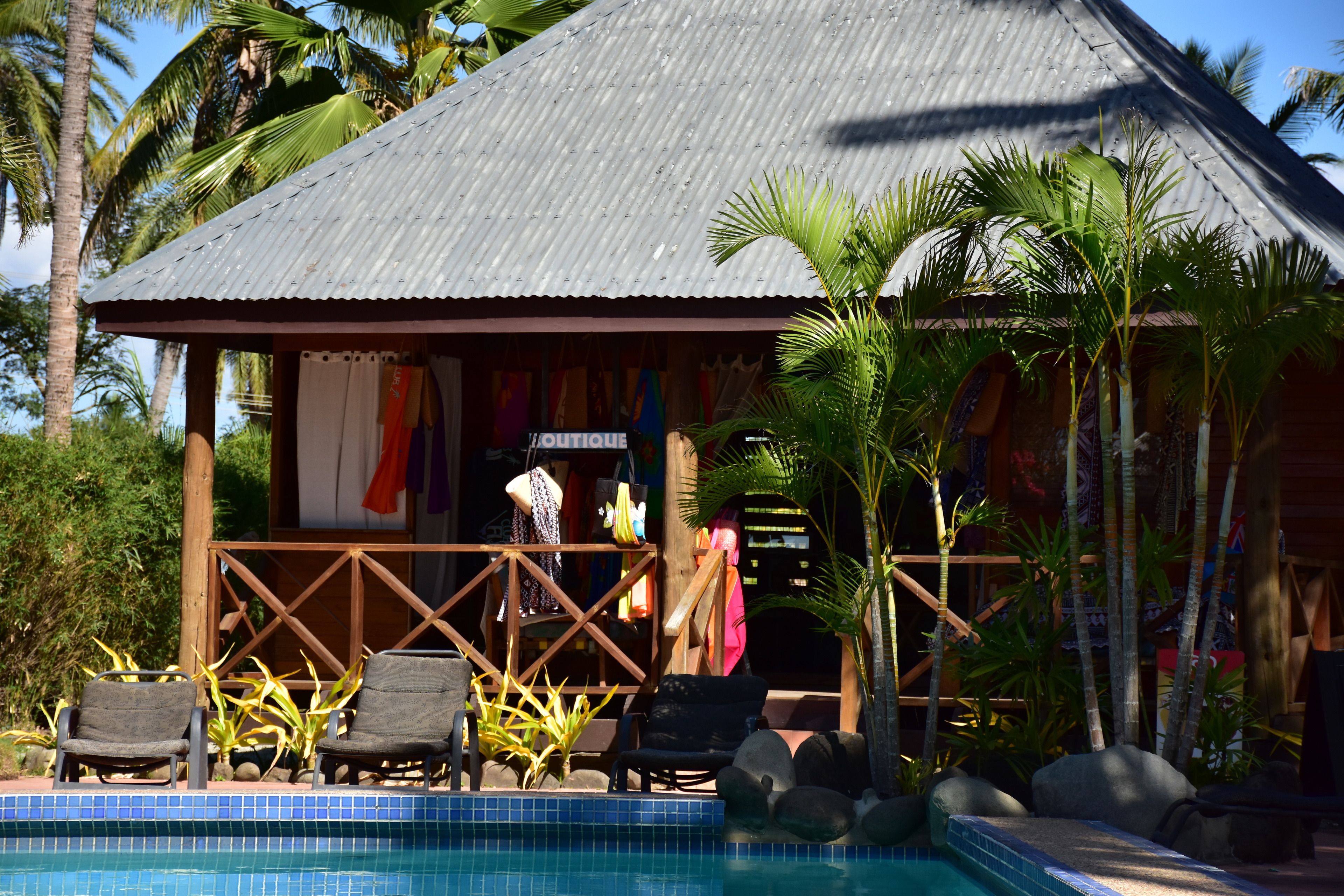 A poolside area with lounge chairs, a small hut with a corrugated metal roof, and tropical plants.
