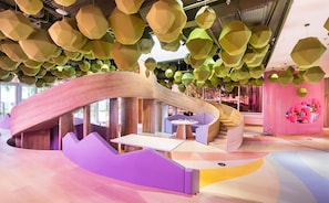A modern interior with a curved wooden structure, a purple seating area, and a pink wall with shelves.