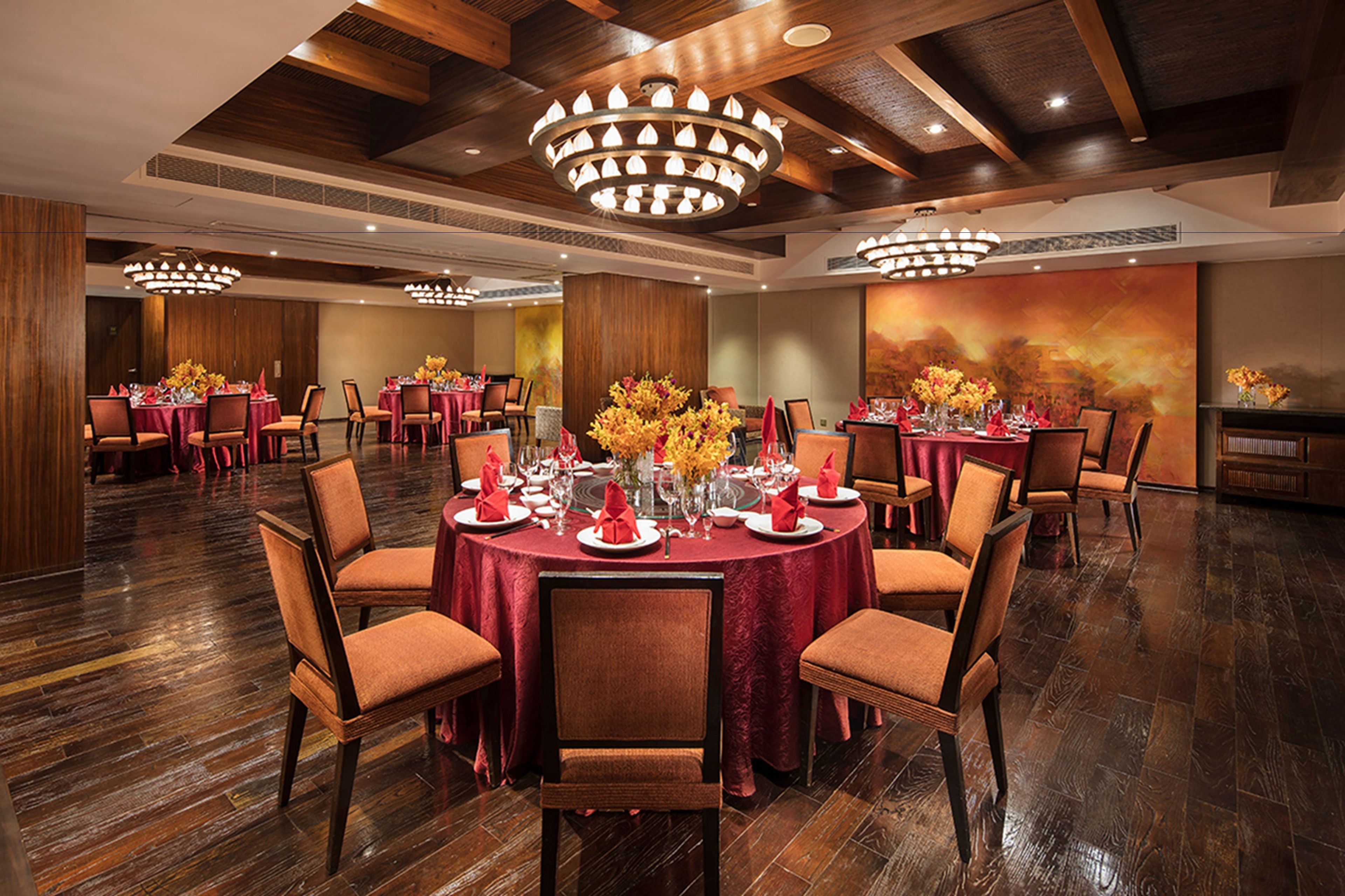 A banquet hall with round tables set for dining, wooden floors, and modern chandeliers.