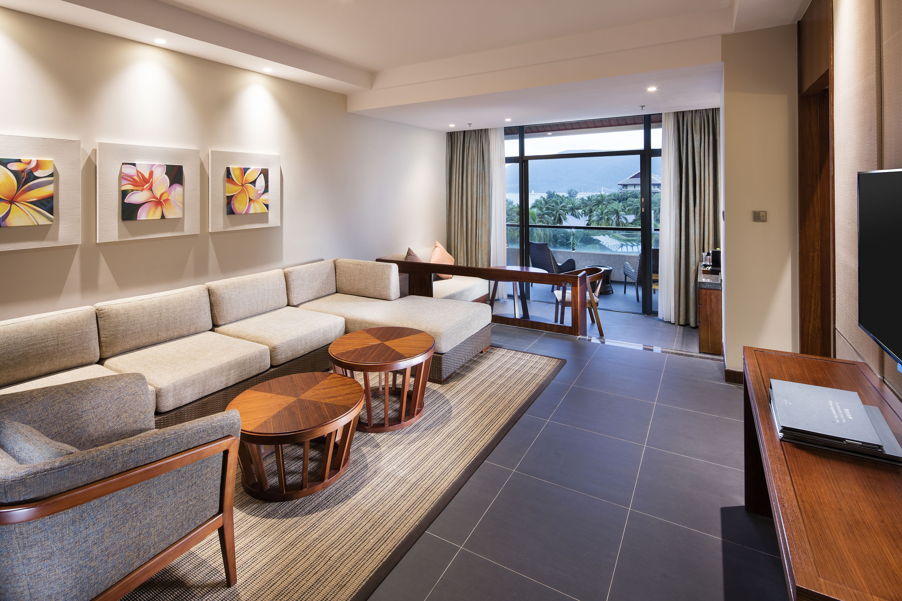 A modern hotel room with a large sofa, two wooden side tables, a flat-screen TV, and artwork on the wall.