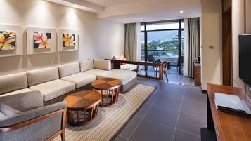 A modern hotel room with a large sofa, two wooden side tables, a flat-screen TV, and artwork on the wall.