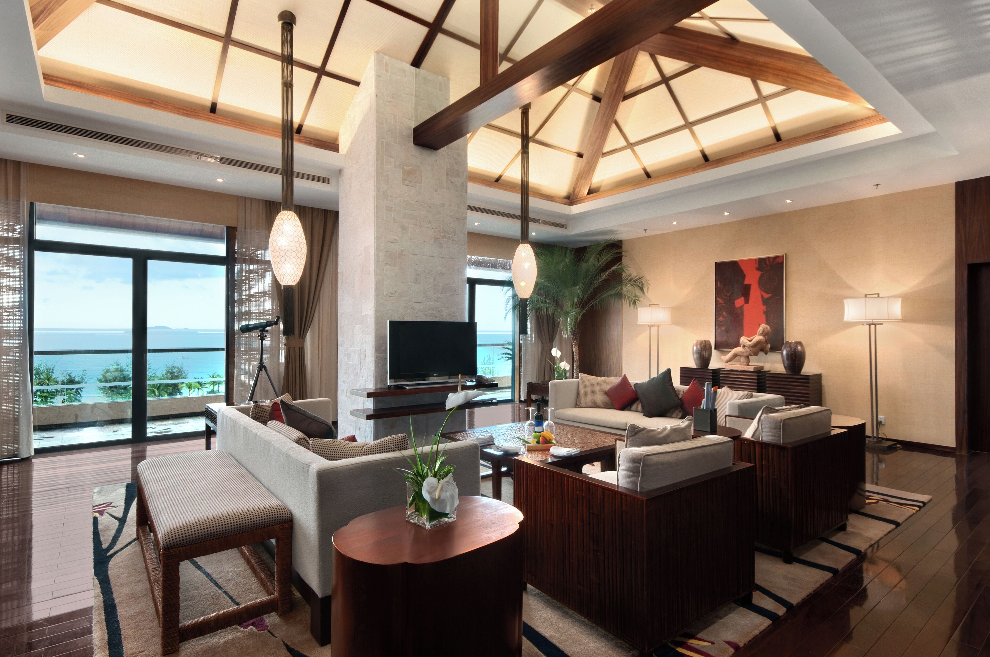 A spacious living room with a large TV, comfortable seating, a wooden coffee table, and a view of the ocean.
