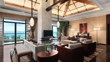 A spacious living room with a large TV, comfortable seating, a wooden coffee table, and a view of the ocean.