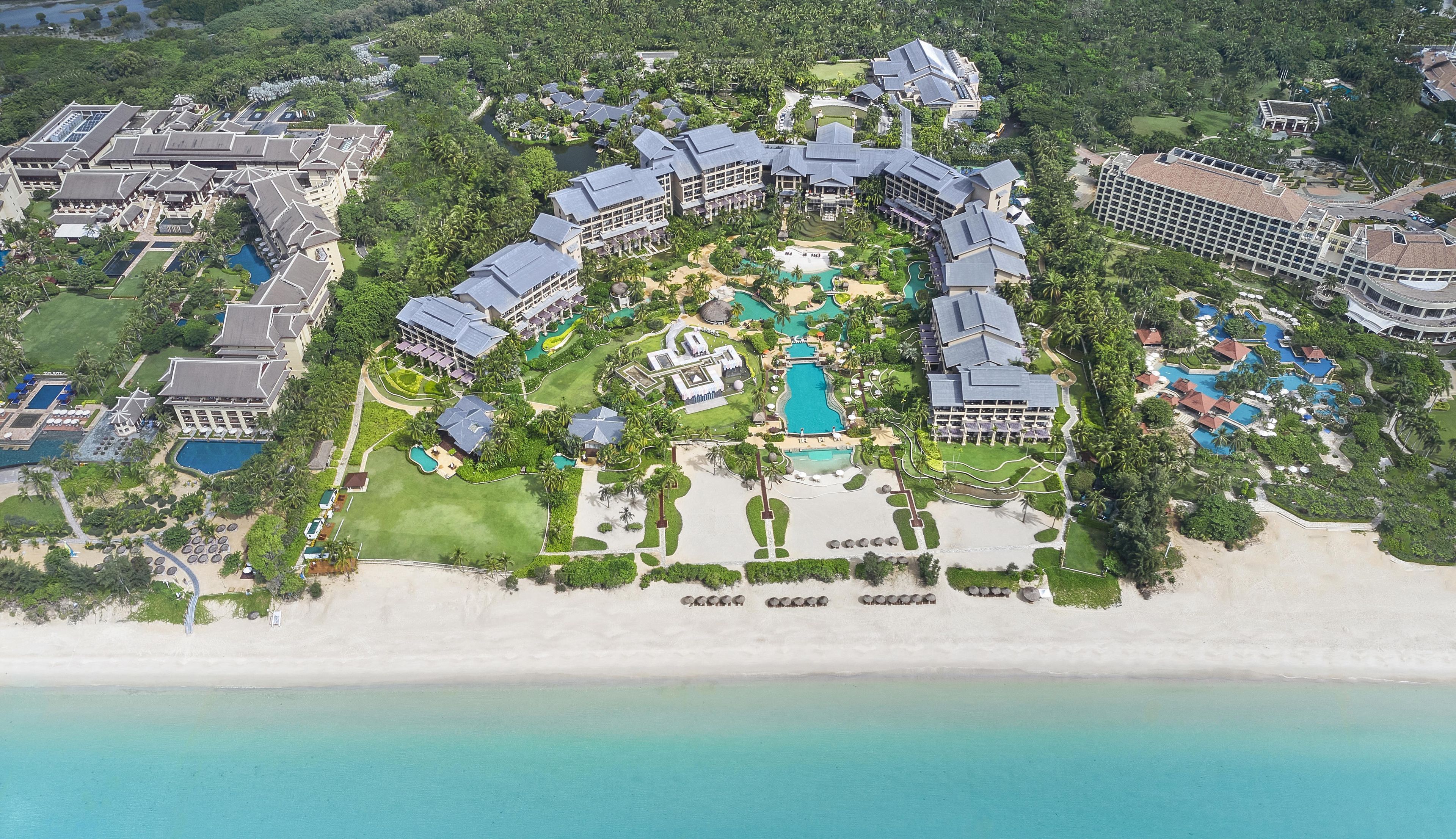 An aerial view of a resort with multiple buildings, a central pool, and a beachfront.