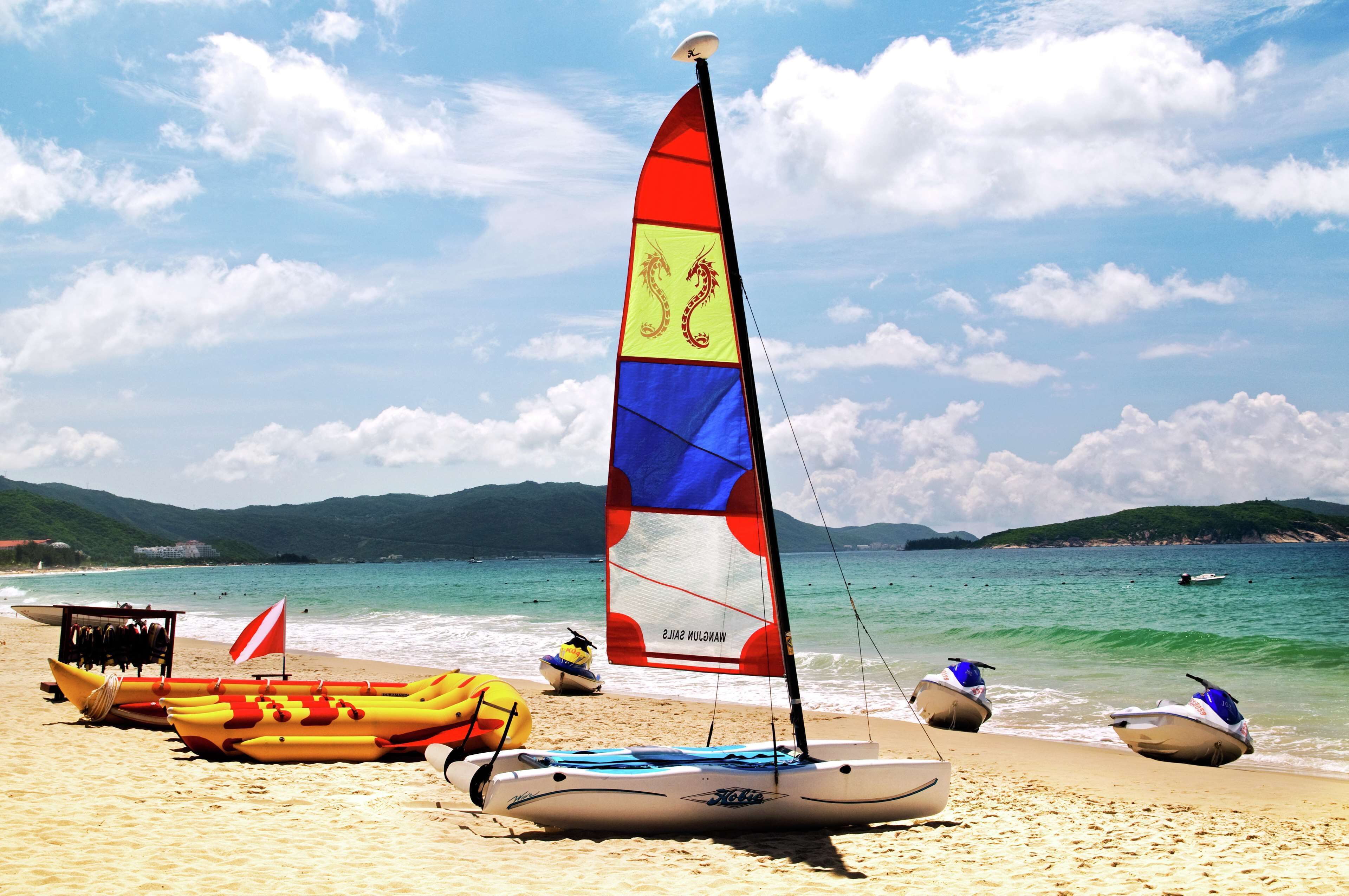 A beach with a sailboat, a jet ski, and a lifeguard stand.