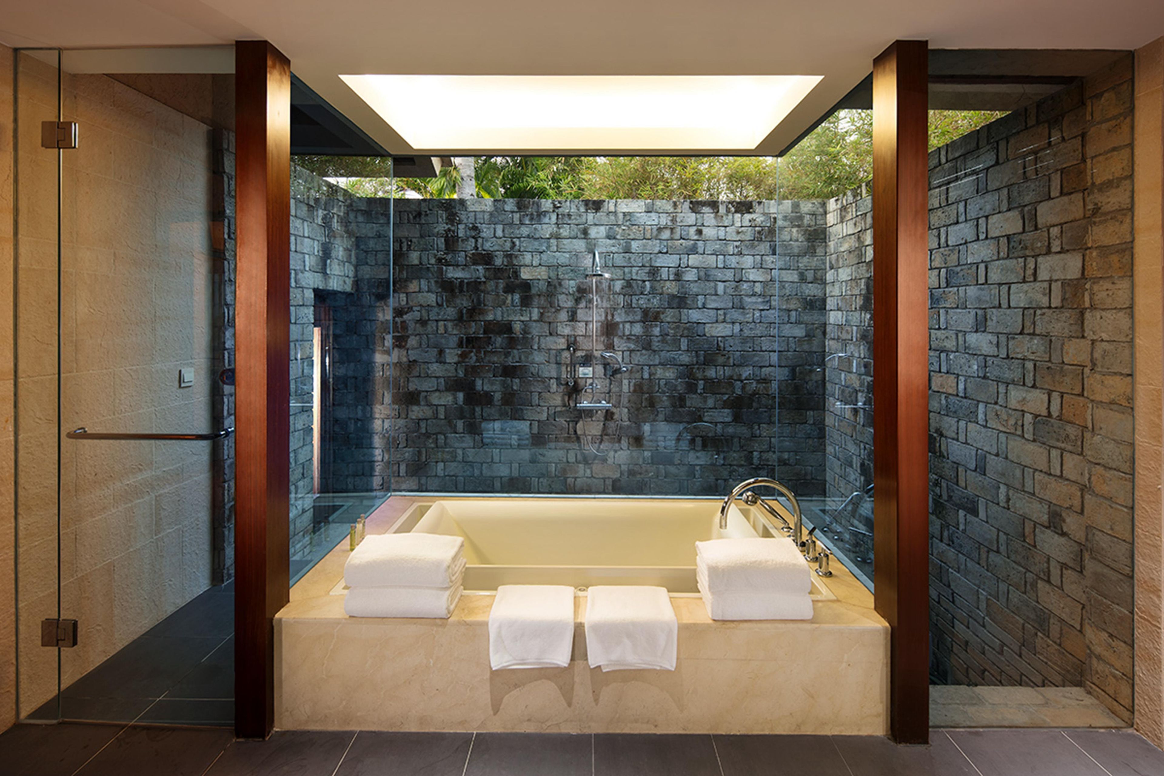 A modern bathroom with a freestanding bathtub, glass shower enclosure, and a brick wall backdrop.