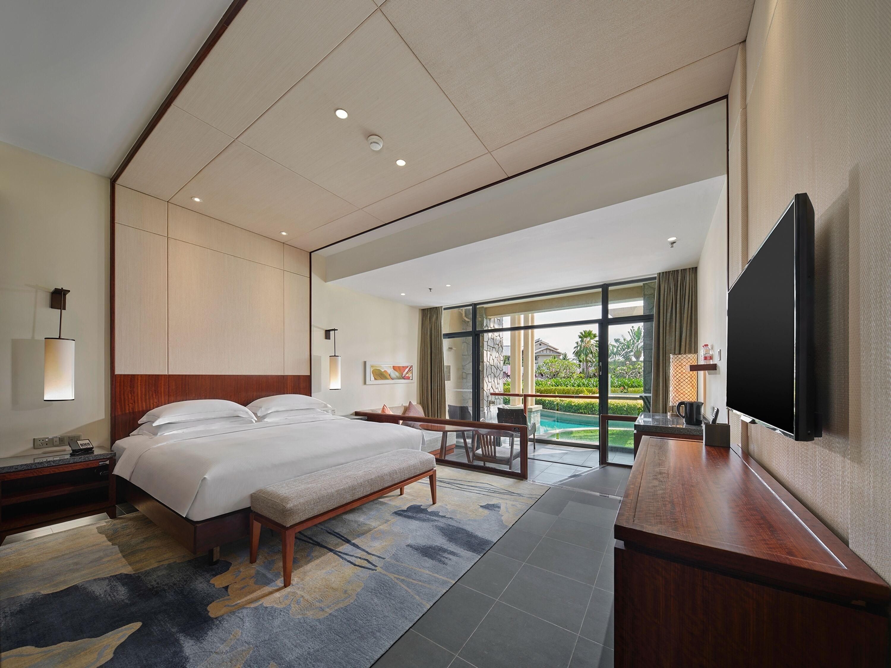 Ein modernes Hotelzimmer mit einem großen Bett, einem Schreibtisch, einem Flachbildfernseher und Blick auf einen Swimmingpool.