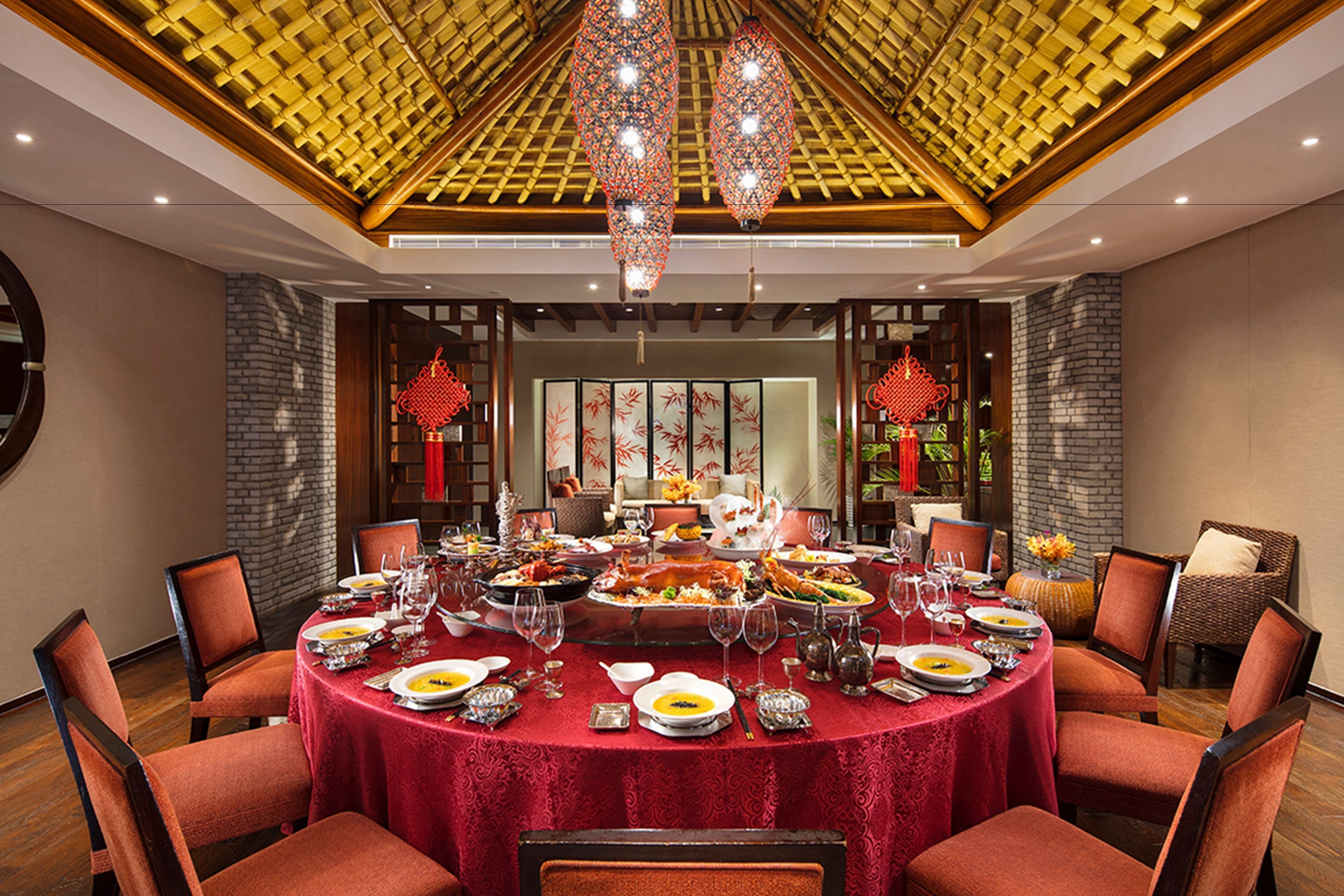A round dining table set with multiple dishes and glasses, surrounded by chairs, in a room with a wooden ceiling and decorative lanterns.