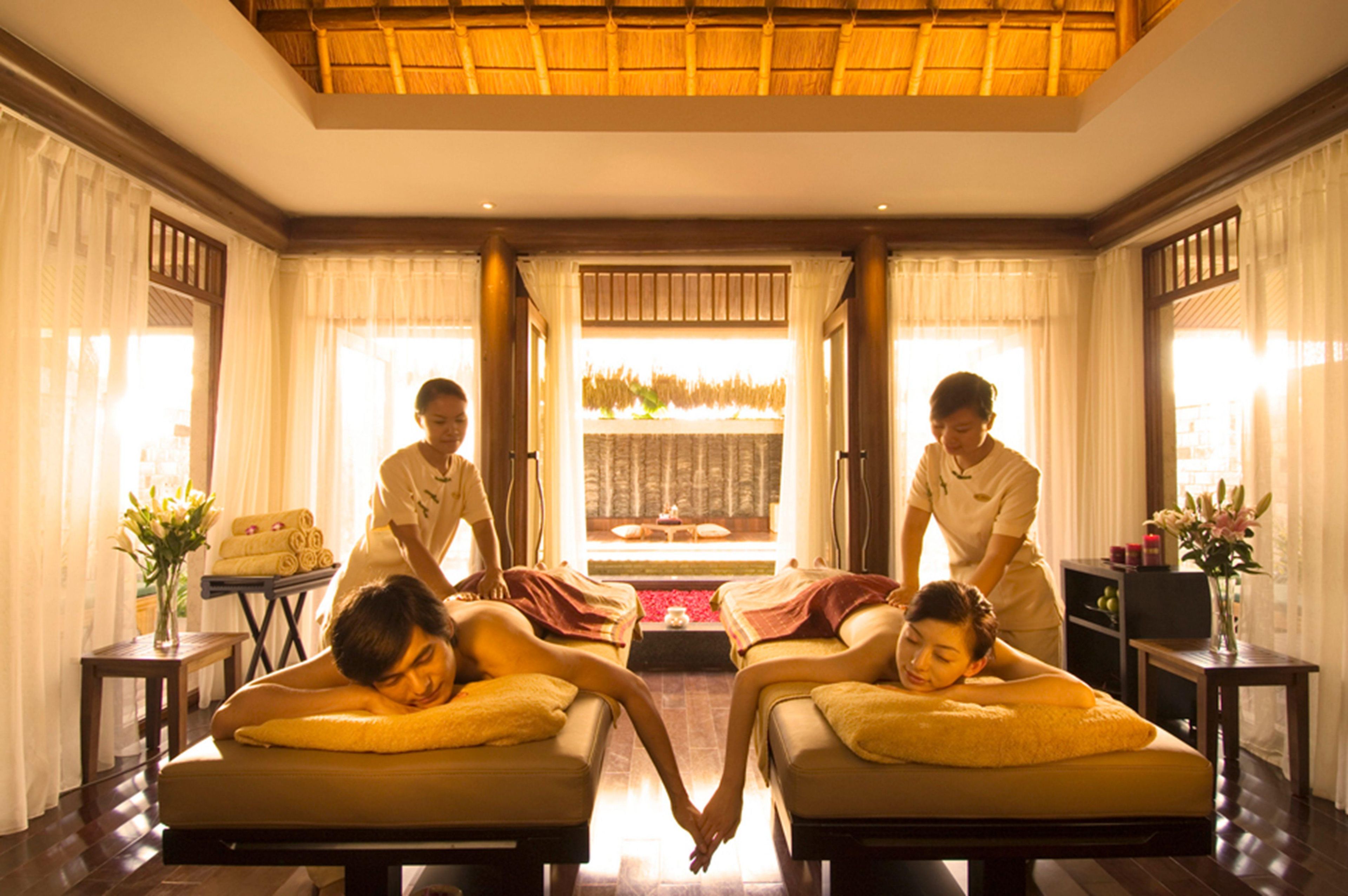 A room with two massage tables, a reception desk, and a view of a garden through a window.