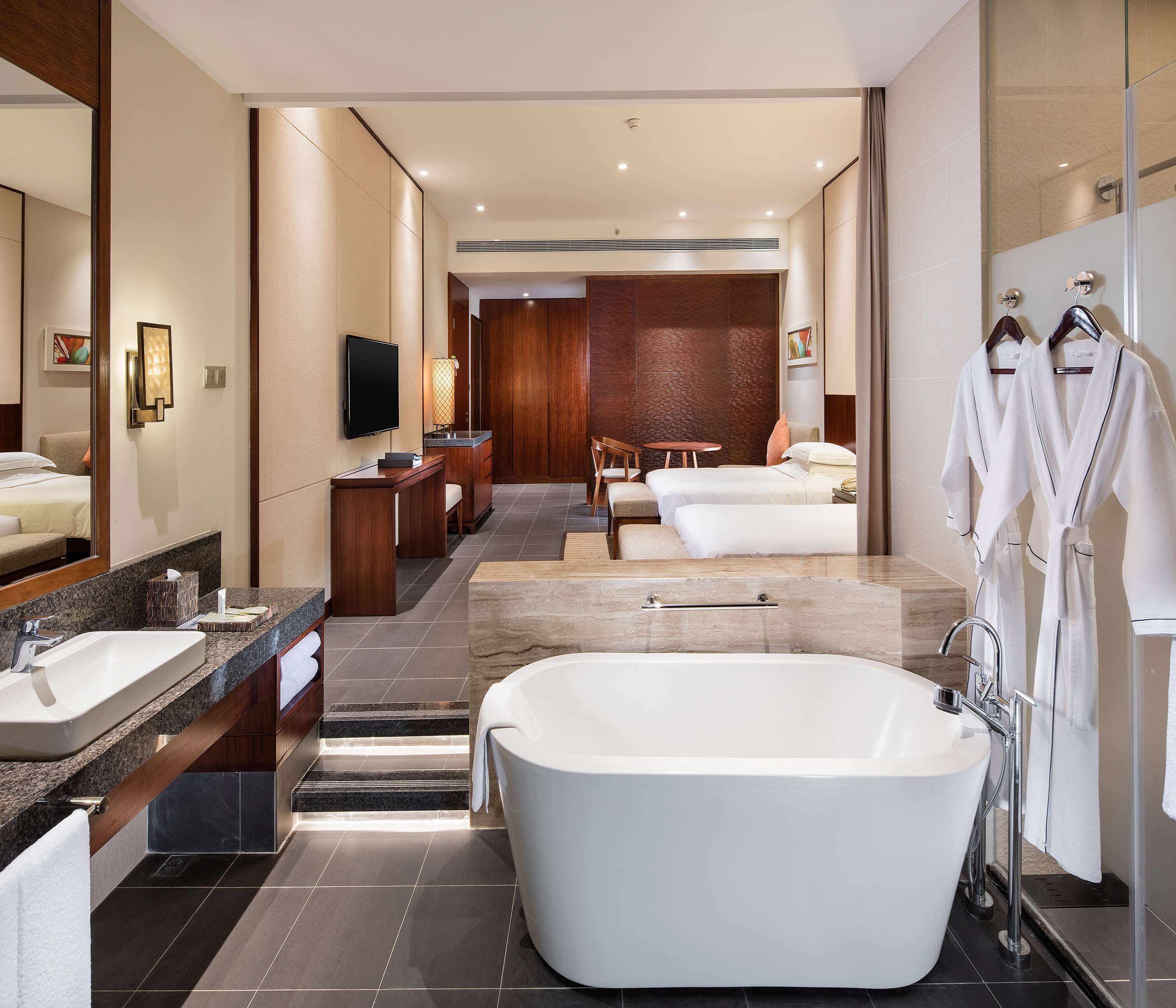 A modern hotel bathroom with a large bathtub, a separate shower area, a vanity with a sink, and a seating area with a table and chairs.
