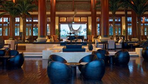 A spacious lobby with high ceilings, large windows, and a central seating area with modern chairs and a decorative sculpture.