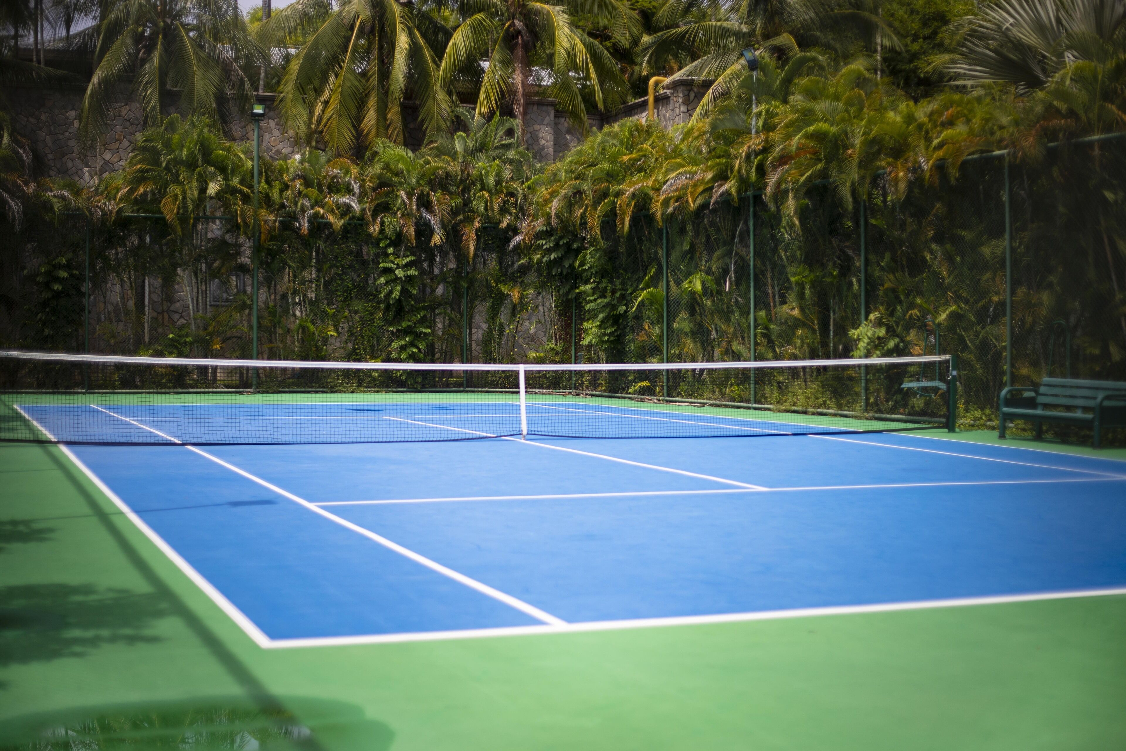 A tennis court with a net, surrounded by lush greenery and a stone wall.