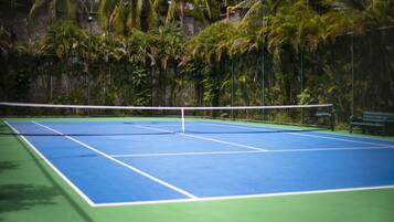 A tennis court with a net, surrounded by lush greenery and a stone wall.