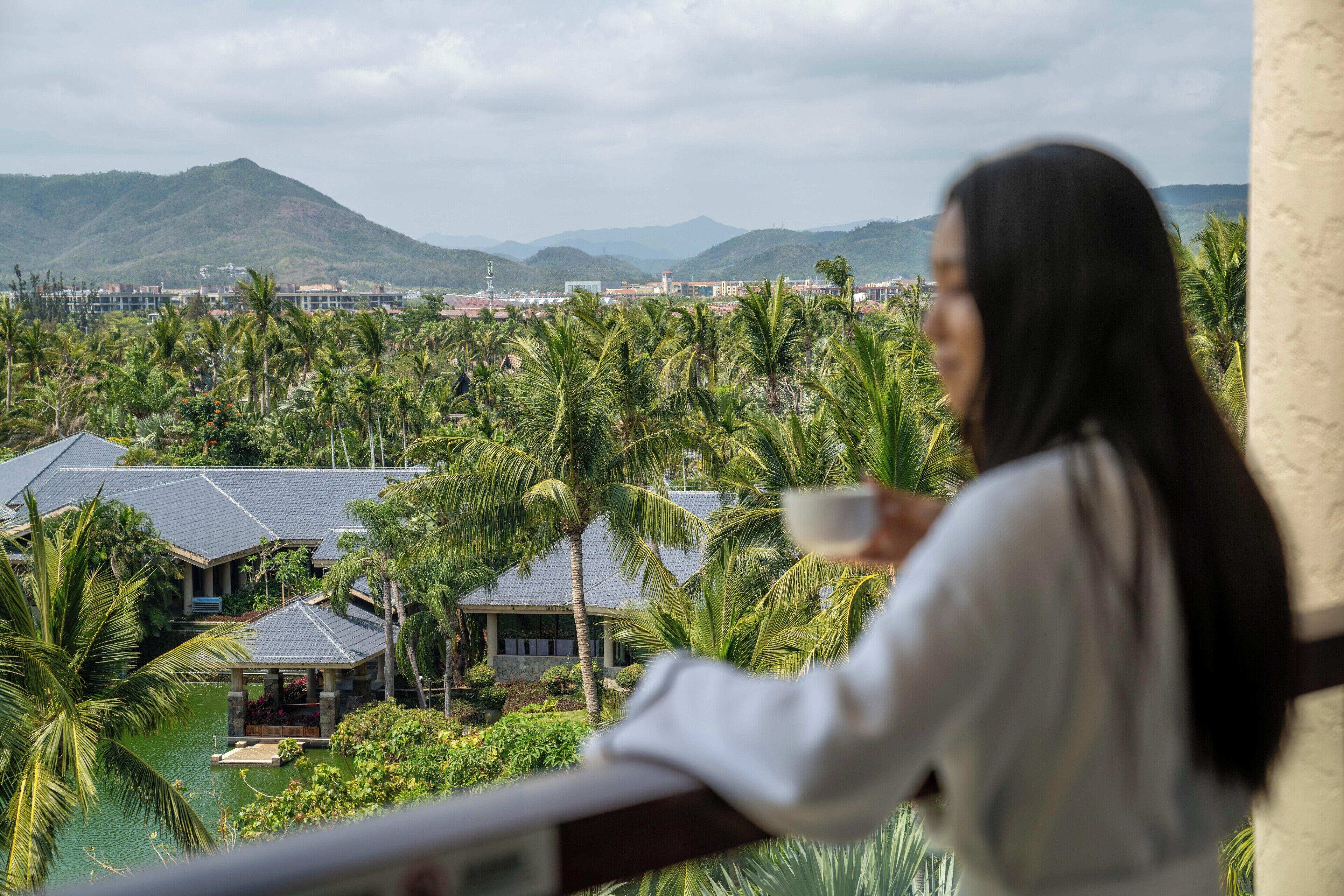 Una persona observa una zona turística con palmeras, una piscina y vistas a montañas distantes.