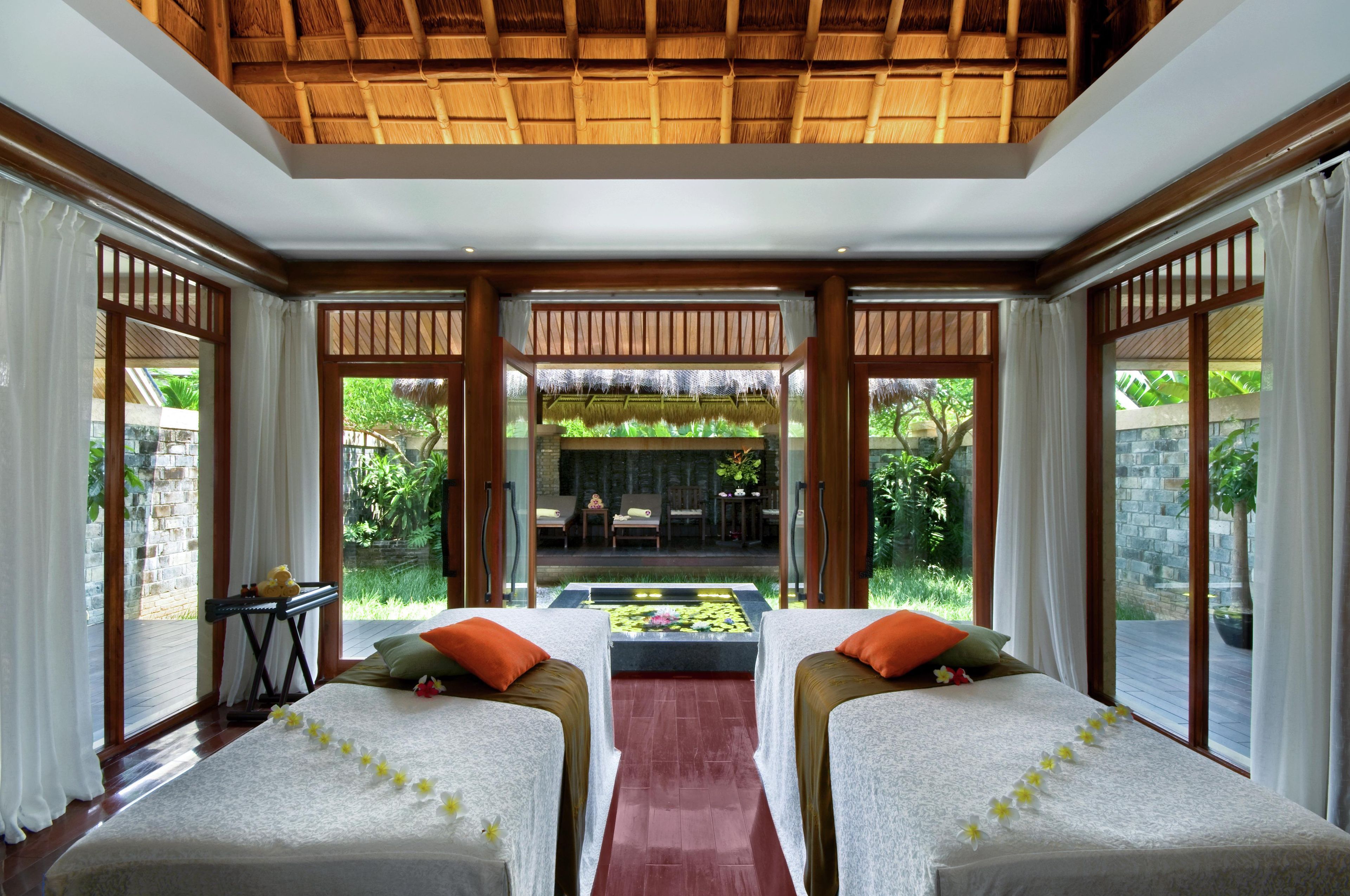 A room with two beds, a view of a garden, and a thatched roof.
