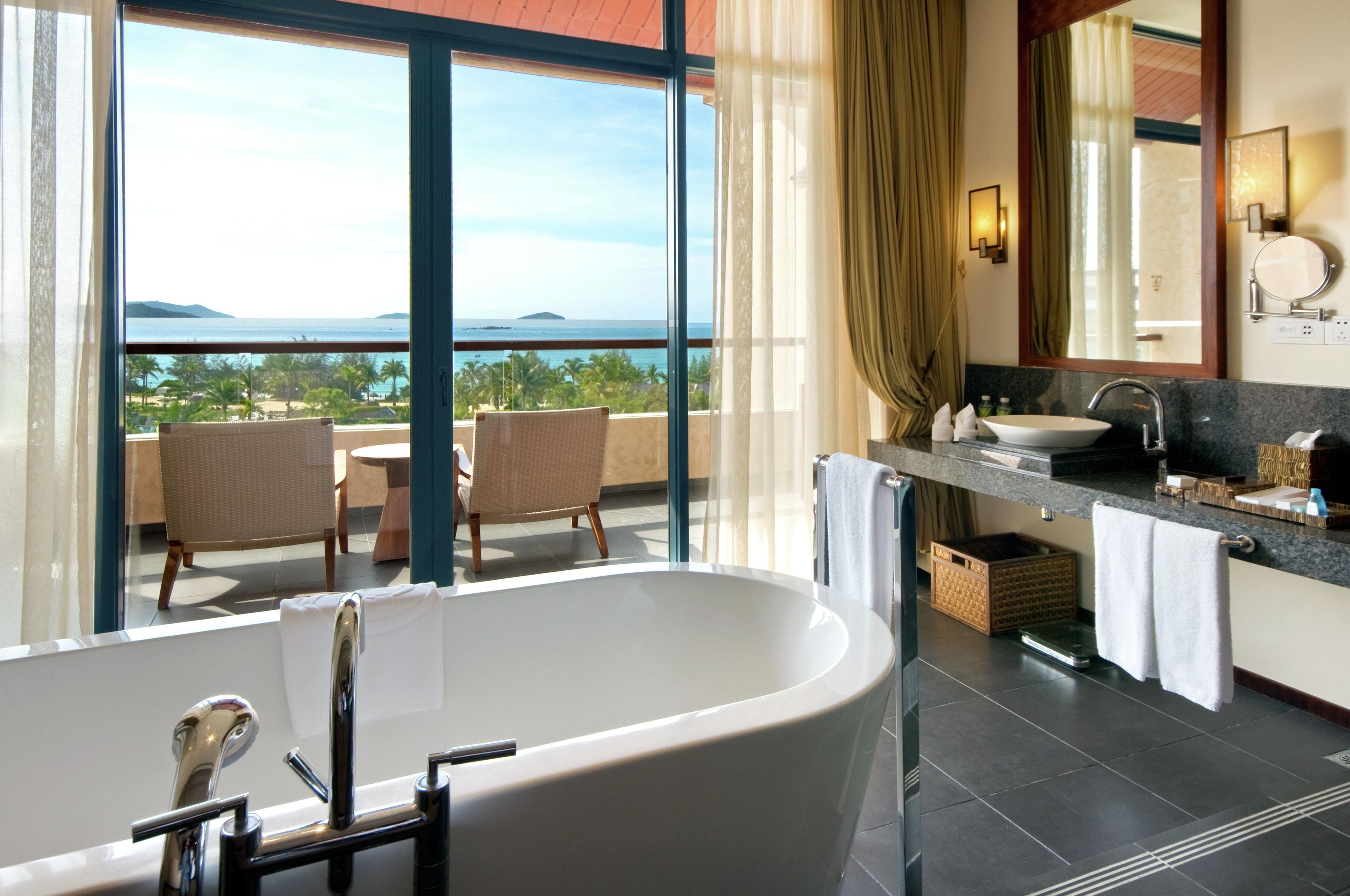 A bathroom with a bathtub, a sink, and a large window offering a view of the sea.