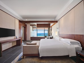 A modern hotel room with a large bed, a flat-screen TV, a seating area, and a view of the ocean.