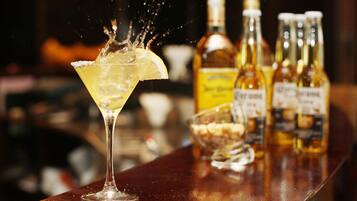 A cocktail with a lemon slice on the rim, a bottle of whiskey, and several bottles of liquor on a bar counter.