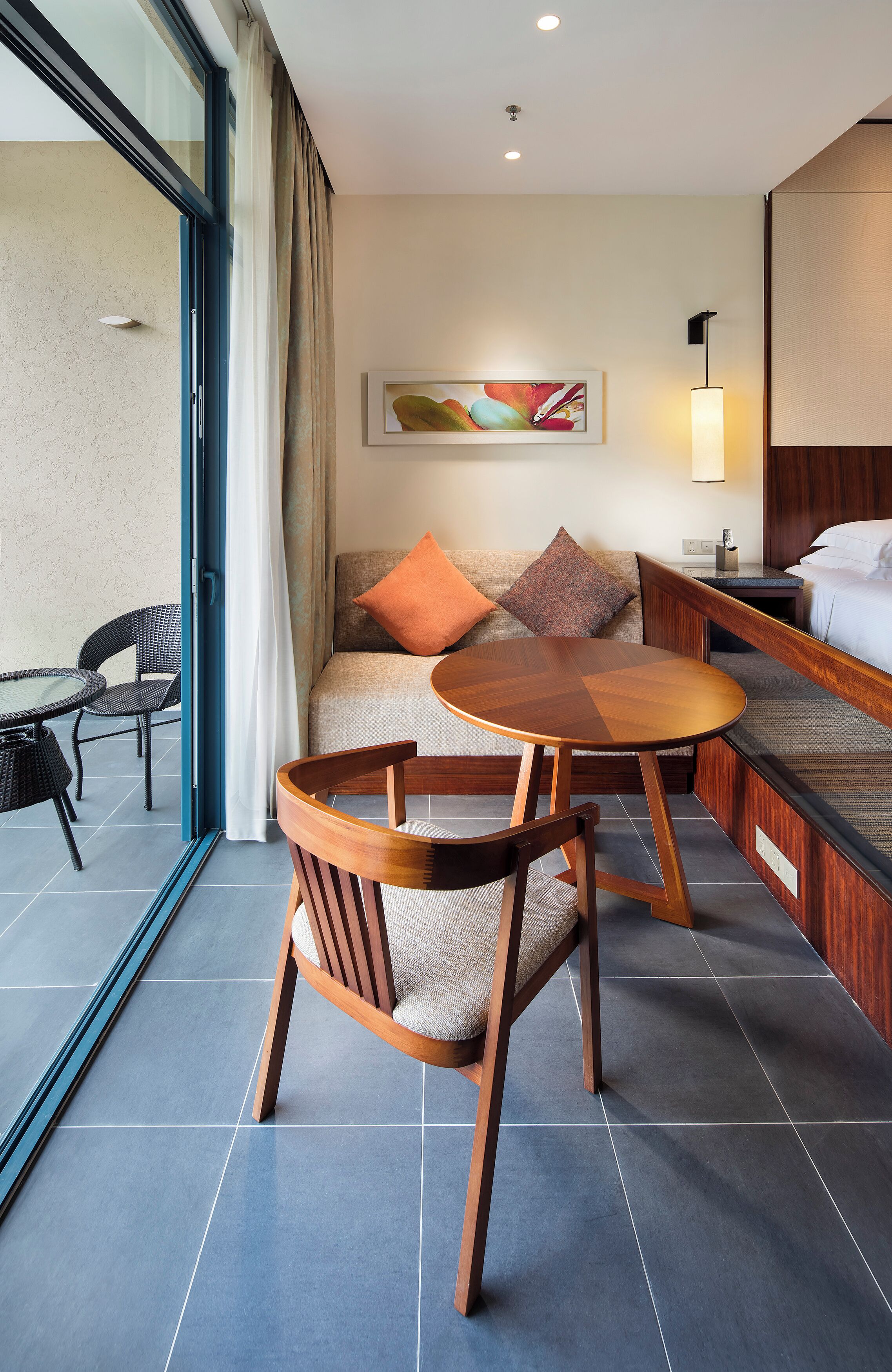 Habitación de hotel con sofá, dos sillas de madera, una mesita redonda, una cama y un cuadro en la pared.