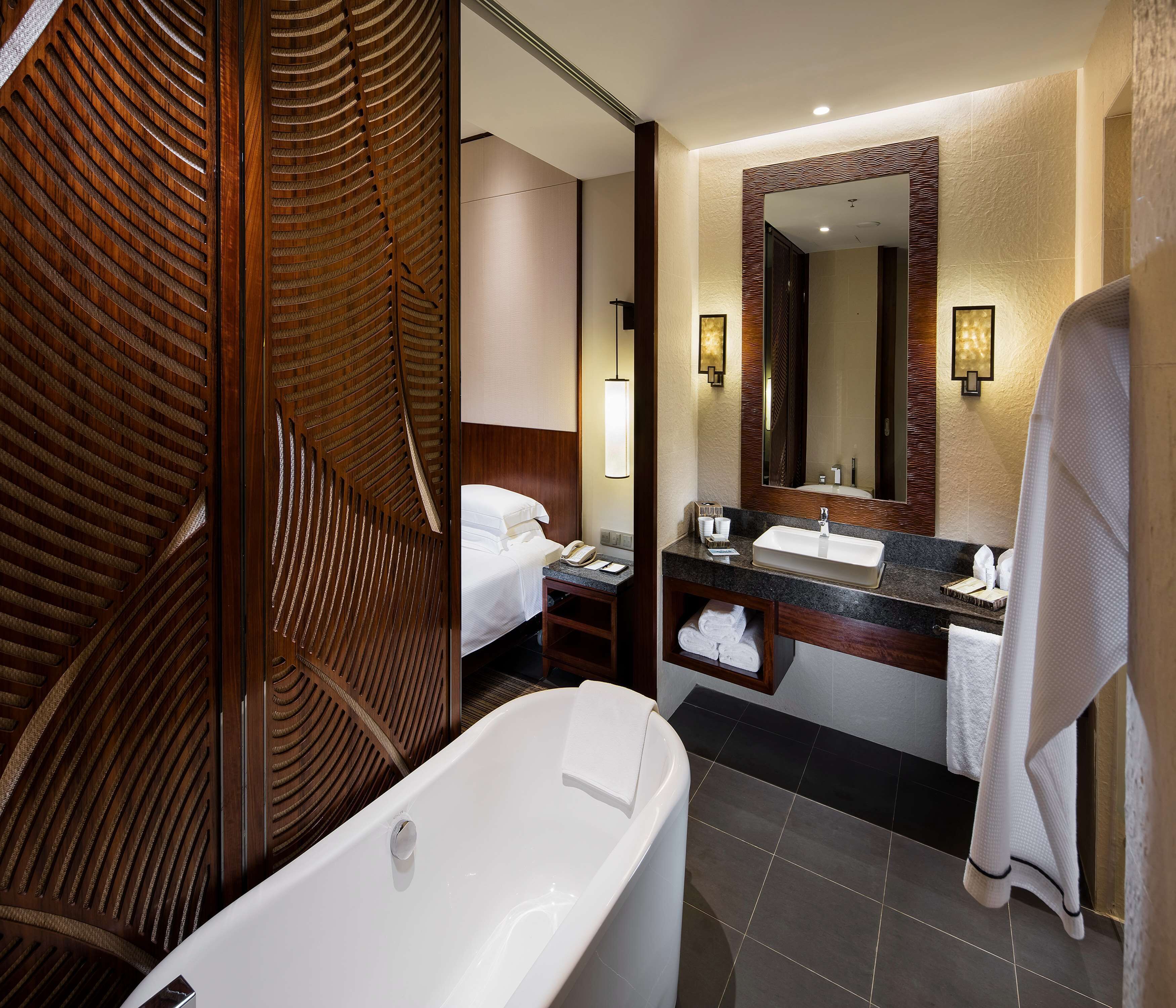 A modern bathroom with a large bathtub, a wooden panel wall, a large mirror, and a vanity with a sink and towel rack.