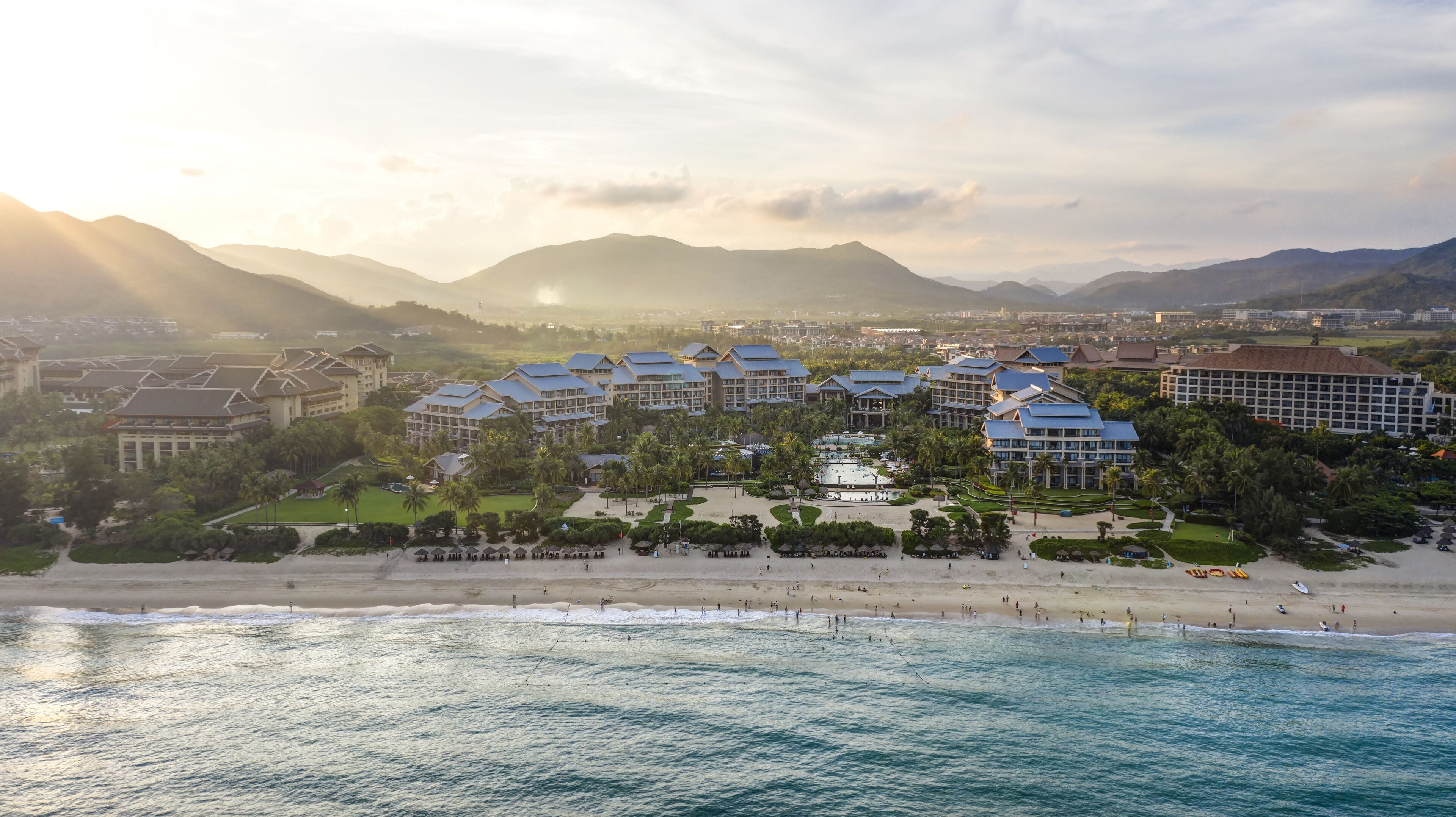 A resort with multiple buildings, a beach, and mountains in the background.