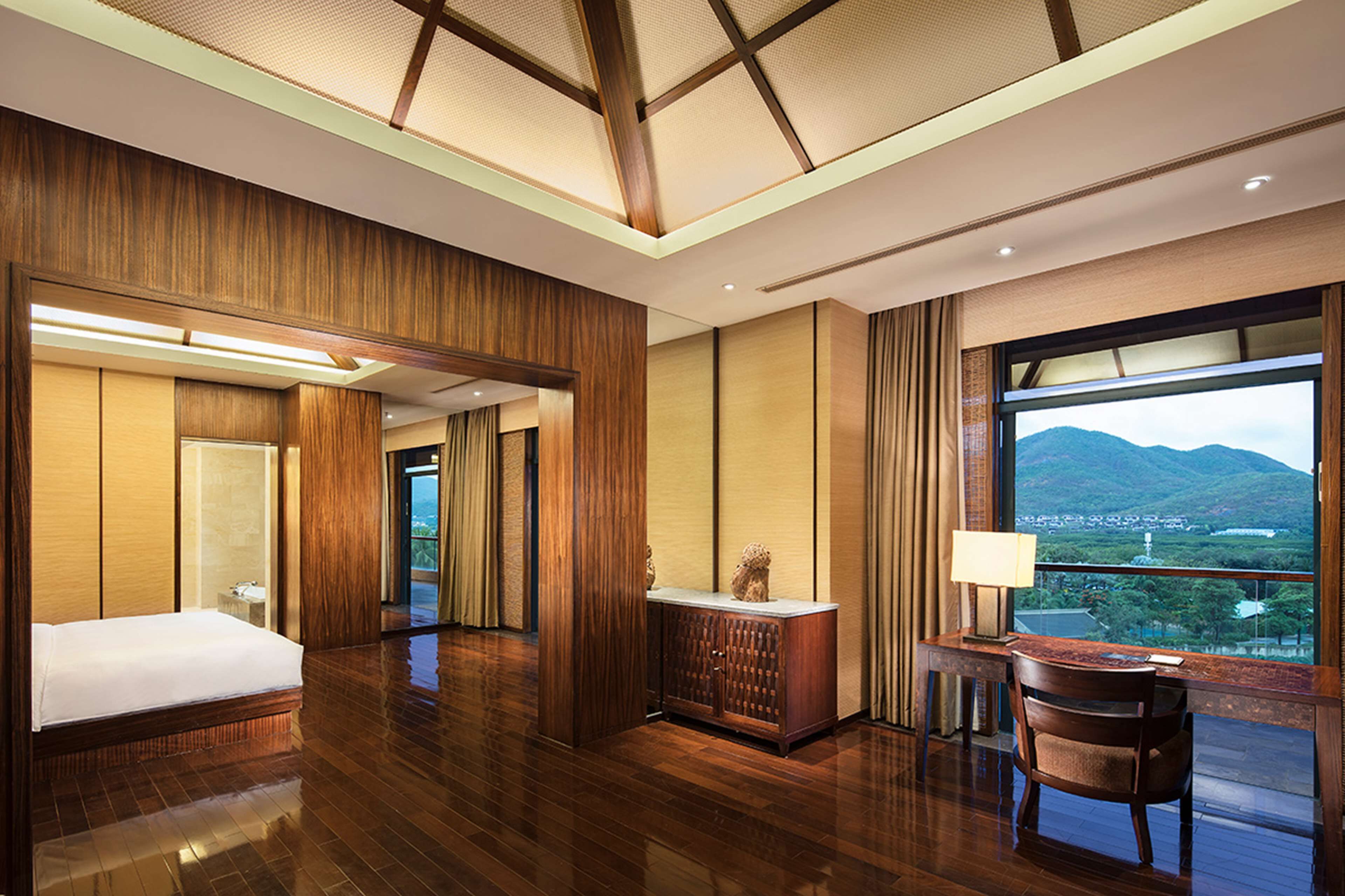 Une chambre d’hôtel avec un grand lit, un bureau avec une lampe et une vue sur les montagnes par la fenêtre.