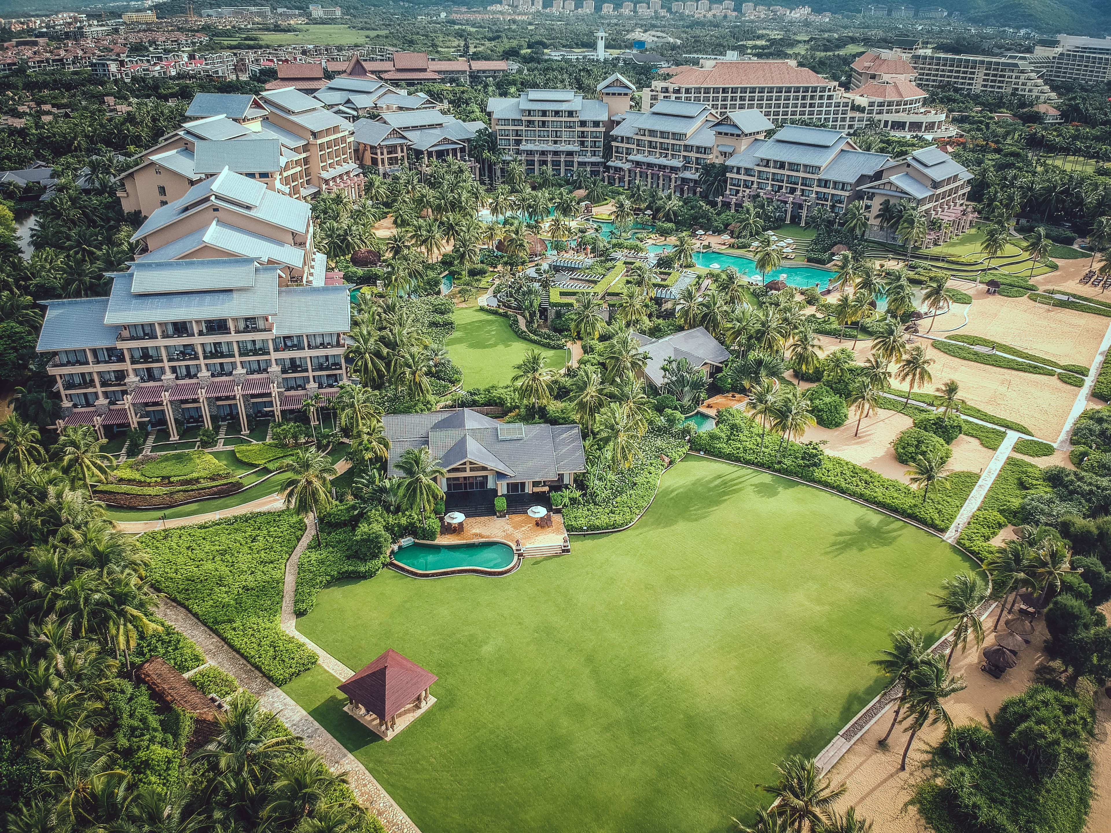 An aerial view of a resort with multiple buildings, a central pool, and surrounding greenery.