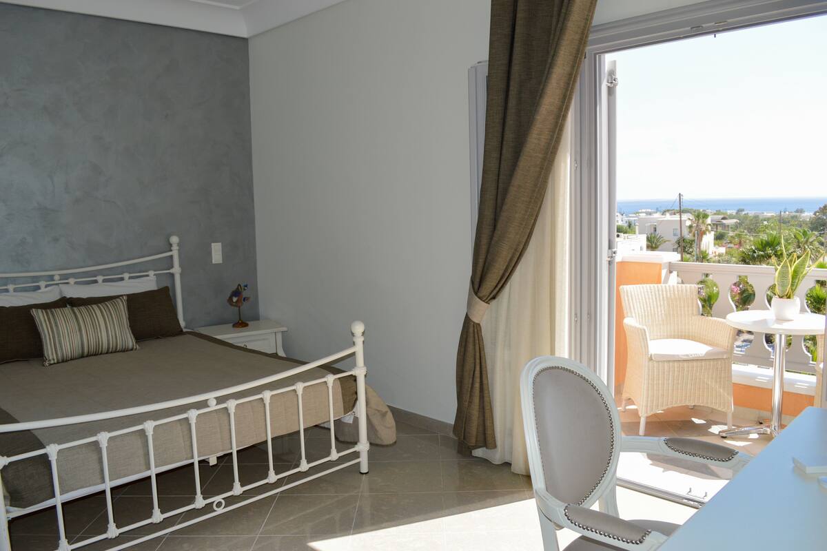 A bedroom with a bed, nightstand, and a balcony with a chair and table.