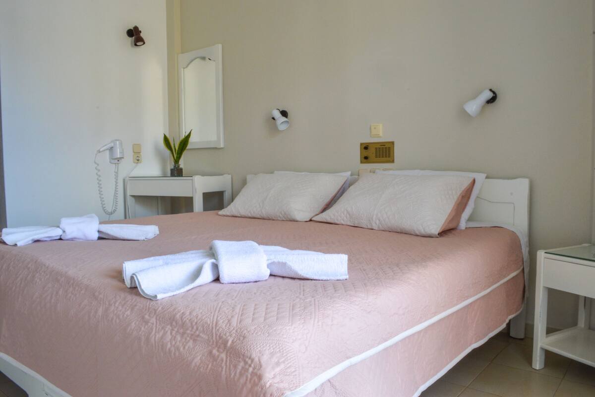 A neatly made bed with pink bedding, a bedside table with a lamp, and a mirror on the wall.