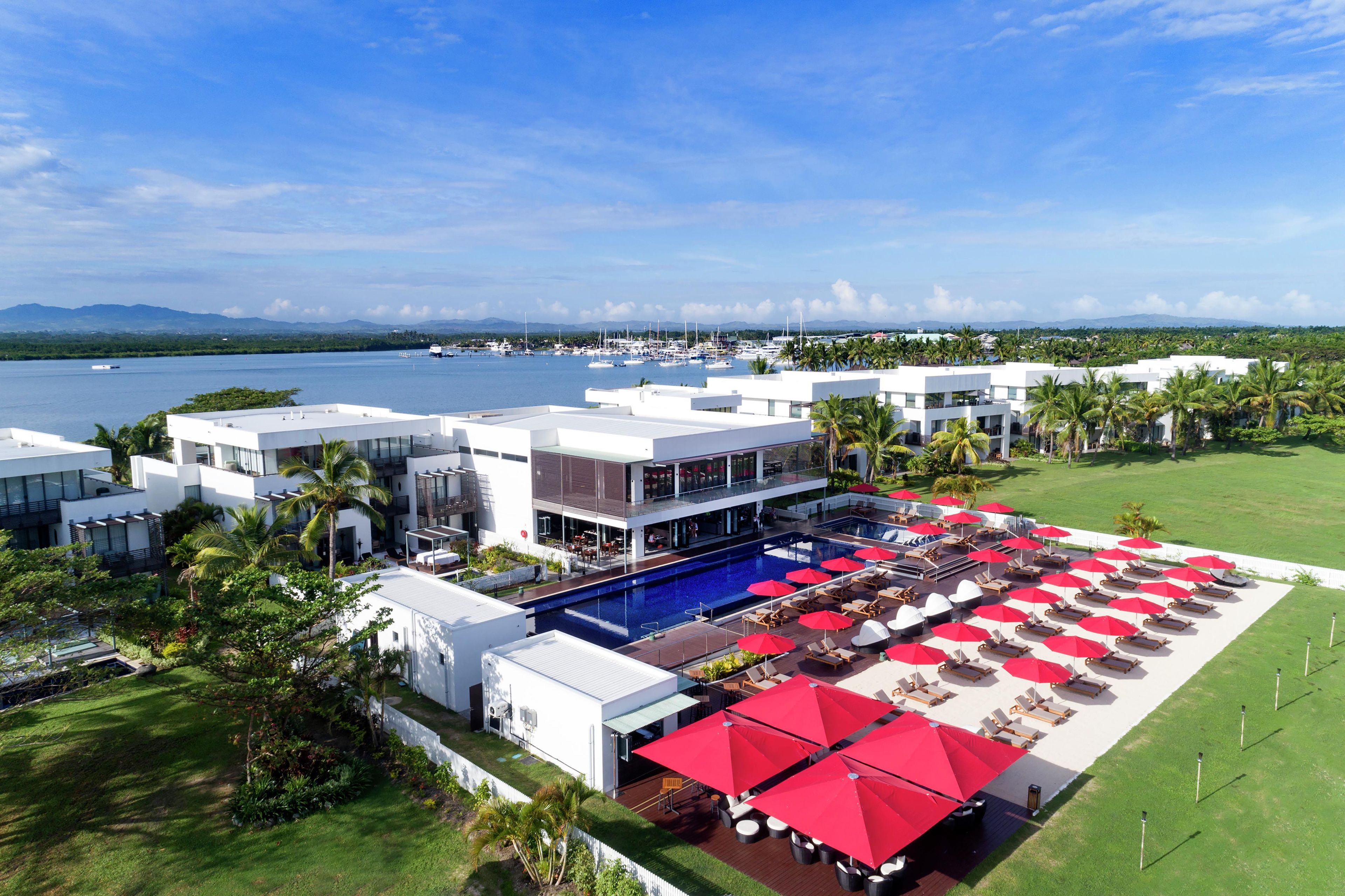 A resort with a pool area, multiple buildings, and a marina in the background.
