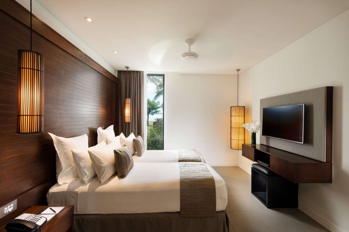 A modern hotel room with a large bed, a flat-screen TV, and a view of greenery outside.